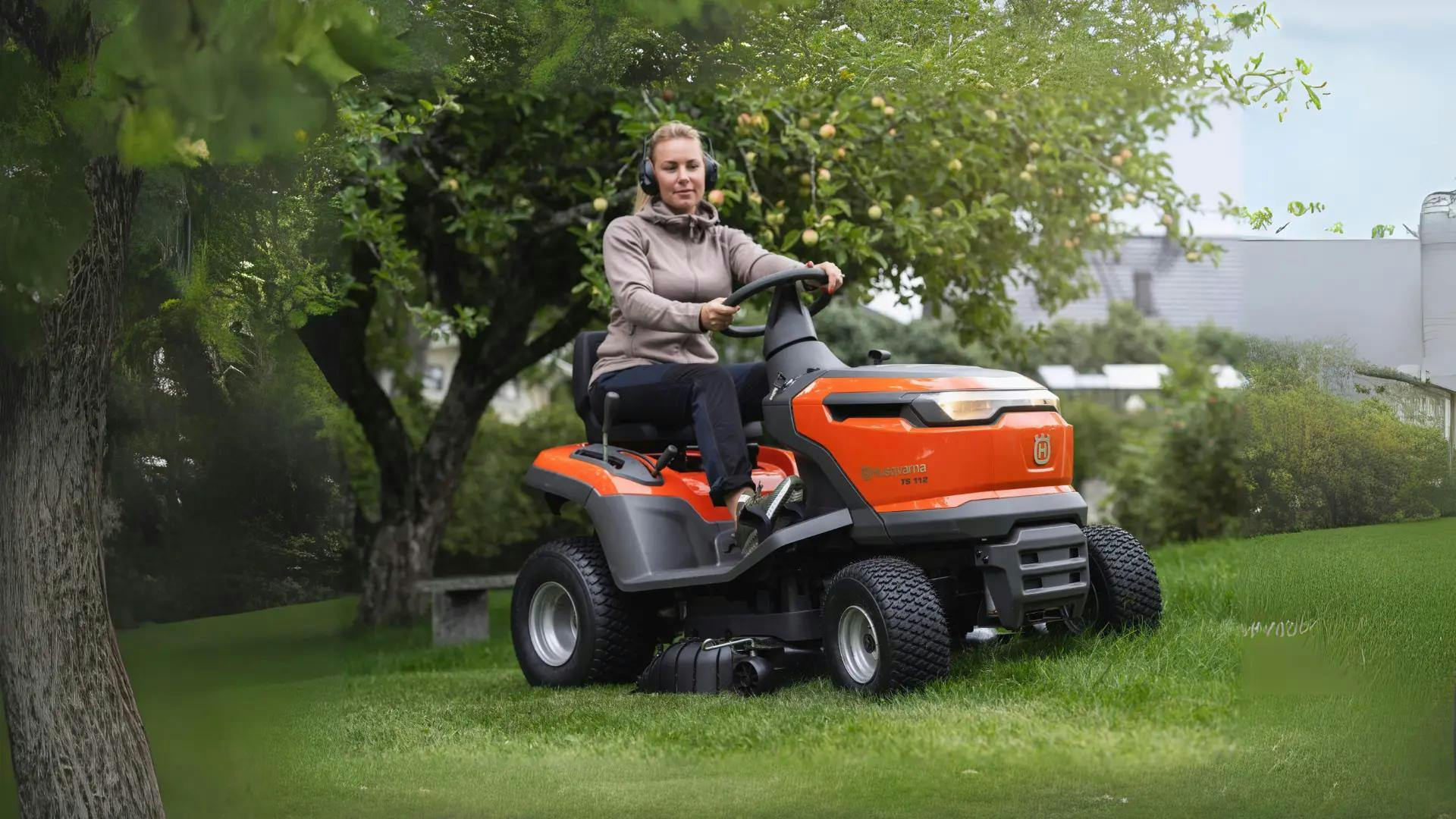 woman sitting on a husqvarna rider underneath lemon tree with protective earmuffs on